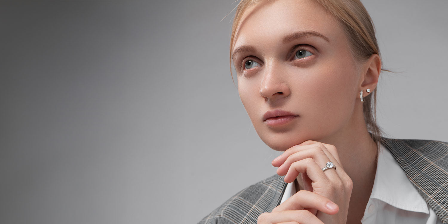 Blonde Frau in grauem Blazer trägt silbernen Ring mit Stein und kleine Ohrstecker